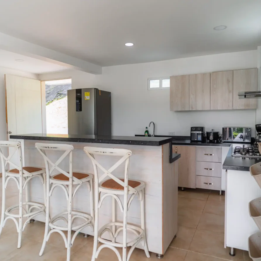 Cocina moderna y luminosa con barra, taburetes y electrodomésticos de acero, ideal para una cabaña en Calima El Darién.