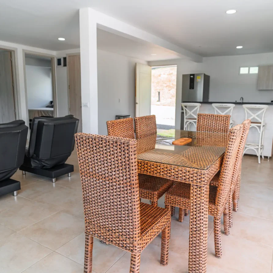 Interior de casa vacacional con mesa de comedor de ratán, sillas y cocina equipada en Calima el Darién.