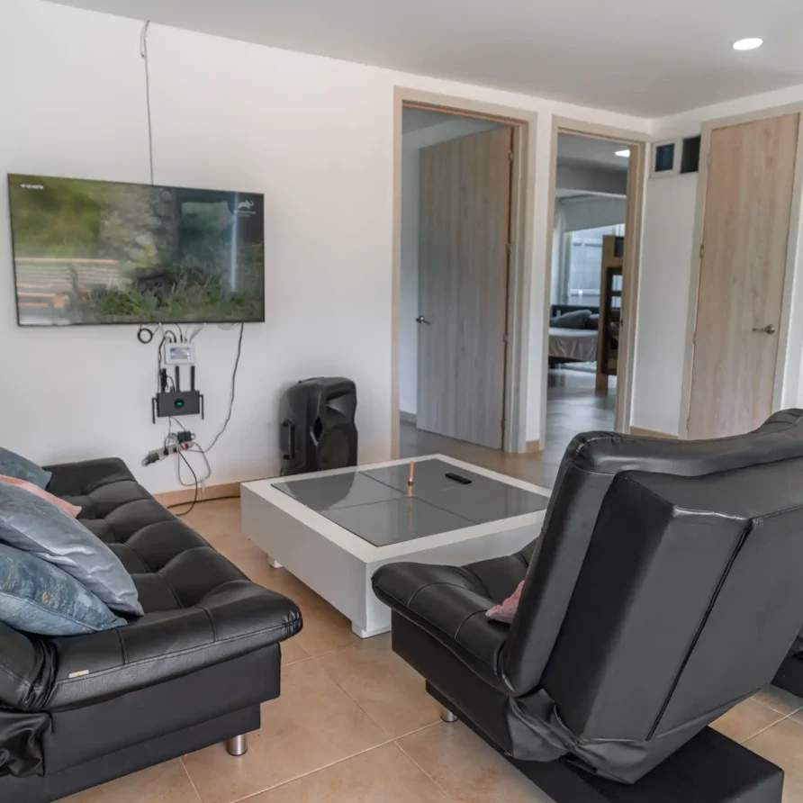 Sala de estar moderna con sofá y sillones de cuero negro, TV y mesa de centro, ideal para una cabaña en Calima.