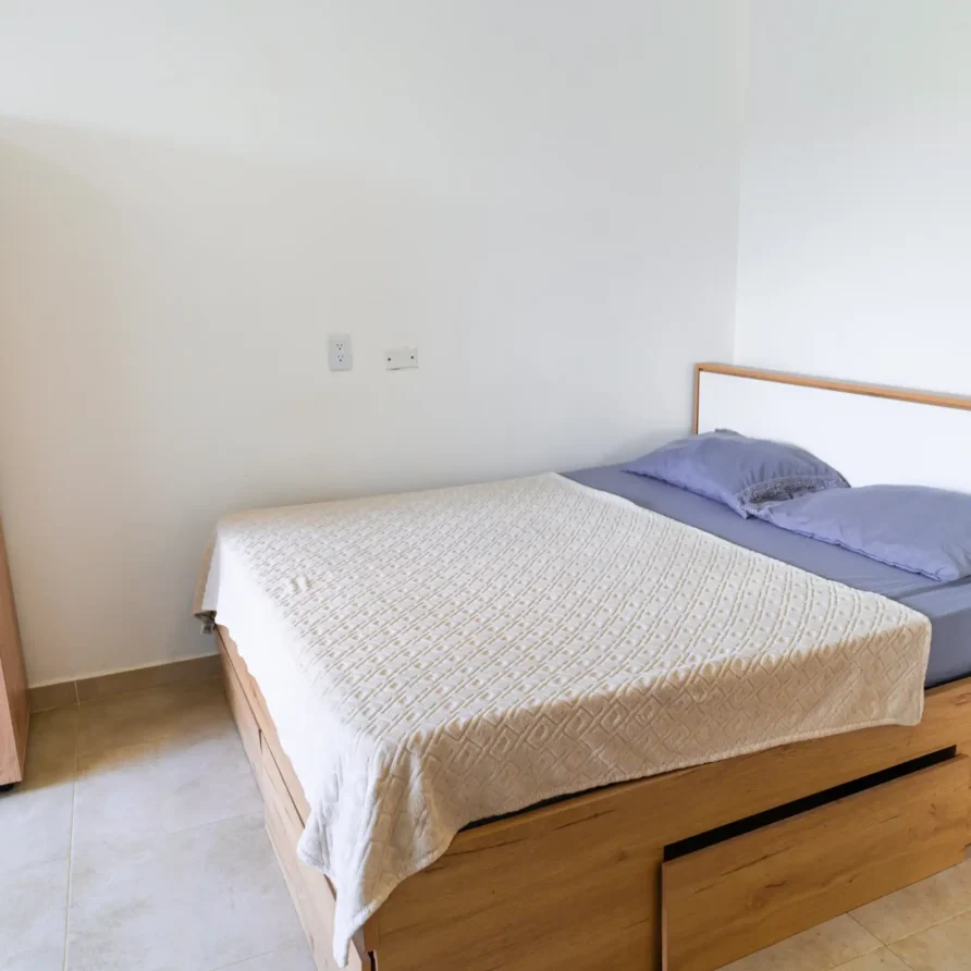 Dormitorio moderno con cama de madera clara, cabecero blanco, cajones de almacenamiento y armario a juego.