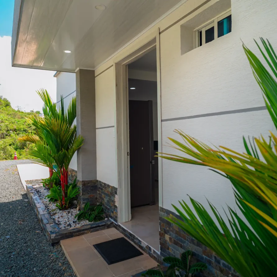 Entrada moderna de cabaña en Calima El Darién, con jardín tropical y camino de gravilla, en un entorno natural verde.