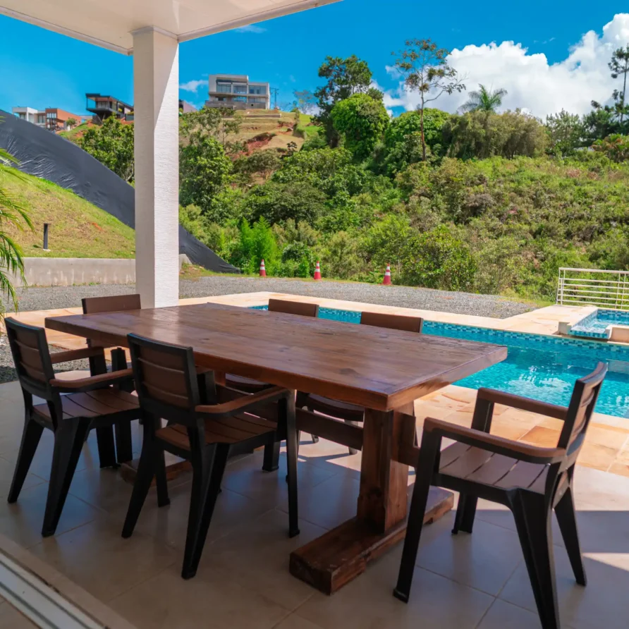 Patio exterior moderno con mesa de madera y sillas junto a piscina, en un entorno tropical de Calima el Darién.