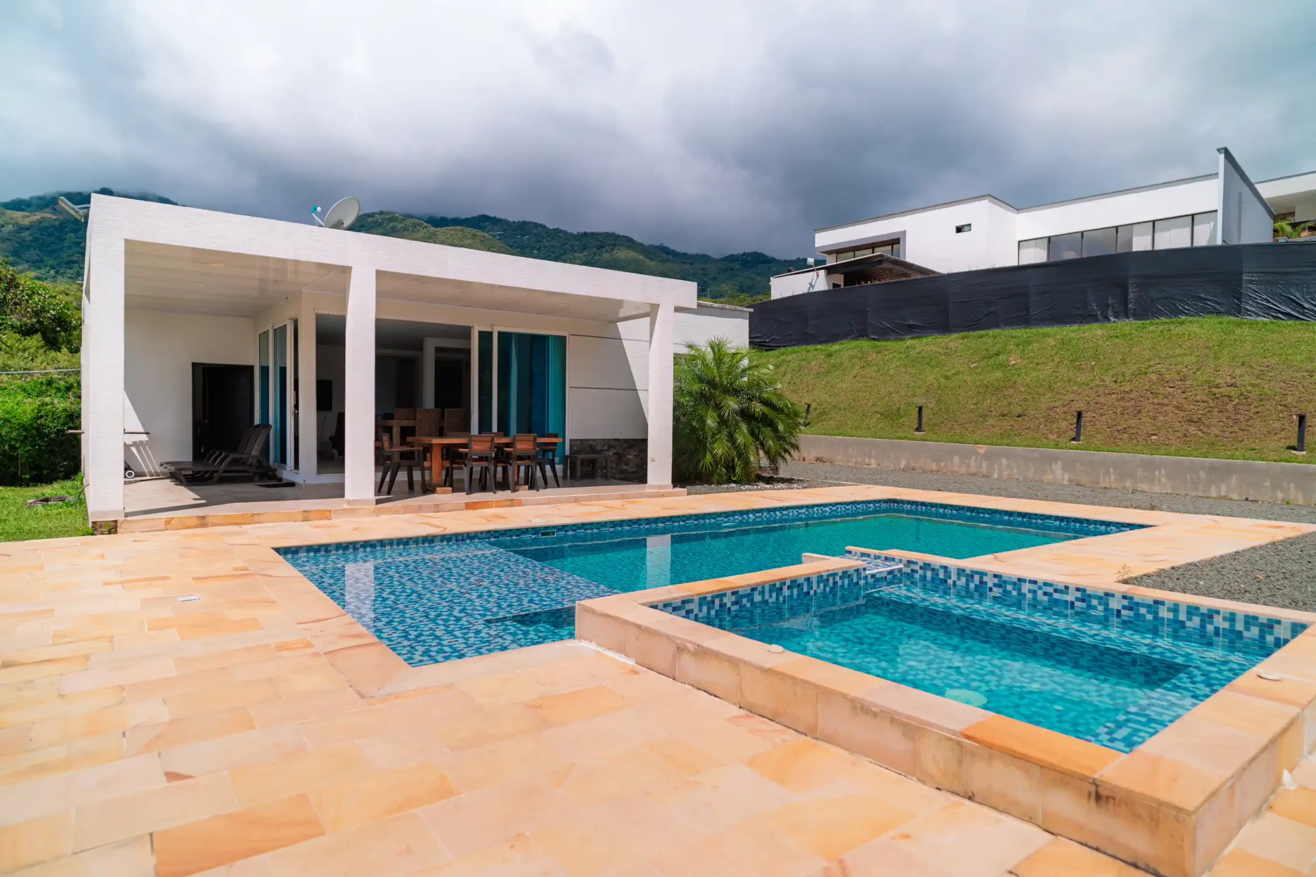 Cabaña moderna con piscina en Calima, patio de baldosas claras, vista a montañas verdes bajo cielo nublado.