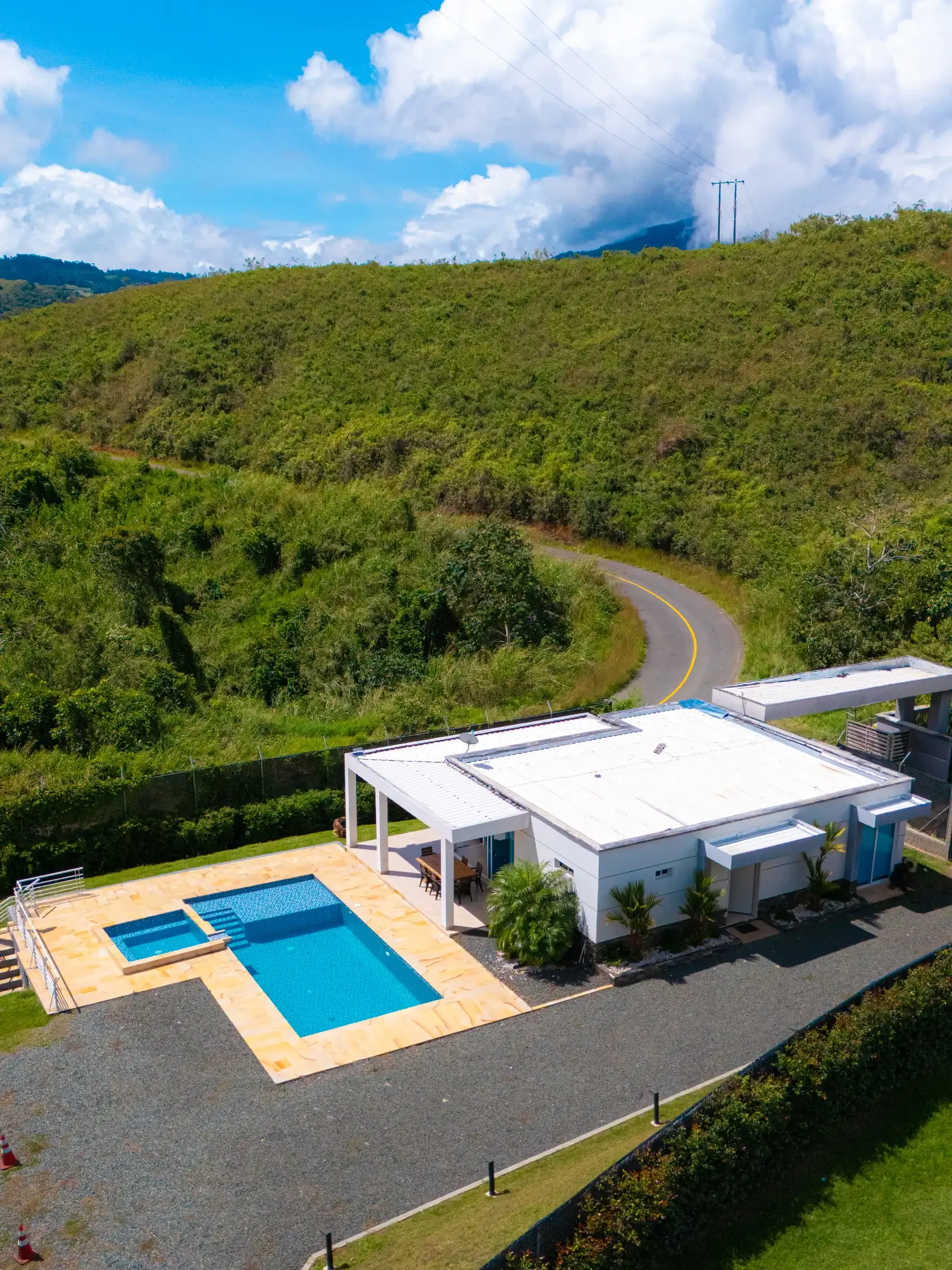 Vista aérea de moderna casa blanca con piscina y jacuzzi en Calima El Darién, rodeada de verdes colinas y naturaleza.